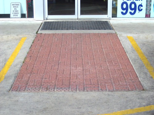 Concrete ramp with bricks for tread from sidewalk entrance to parking lot level. Doorway shown above